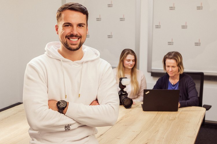 Ein Mann steht vor einem Besprechungstisch, an dem zwei Frauen auf einen Laptop schauen. Foto: Thomas Grimm