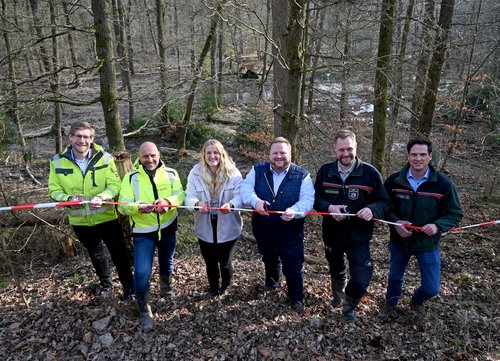 Pressefoto Schwammwald. Foto: Susanne Schulte-Nölle/ Kreis Soest Mit dem symbolischen Durchschneiden eines Flatterbands im Schwammwald-Projektgebiet im Arnsberger Wald am 20. März 2026 wurde es sichtbar: Der erste von vier Bauabschnitten ist fertiggestellt. Zu den Scheren griffen (v. l.) Philipp Büngeler (Abteilungsleiter Umwelt Kreis Soest), Oliver Jürgens (Sauer & Sommer Straßen- und Tiefbau GmbH), Projektleiterin Jennifer Weber (Abteilung Umwelt Kreis Soest), Landrat Heinrich Frieling, Olaf Ikenmeyer (Regionalforstamtsleiter Arnsberger Wald) und Arne Heck (Forstrevierleiter Ruhrverband). Foto: Susanne Schulte-Nölle/ Kreis Soest