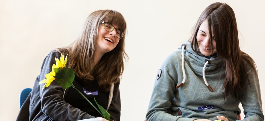 Zwei junge Frauen auf Stühlen mit einem Lächeln im Gesicht. Foto: © Irrsinnig Menschlich