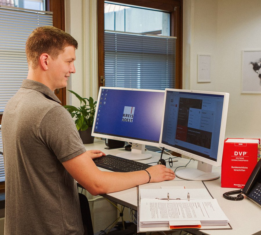 Ein junger Mann bearbeitet einen Antrag, während vor ihm ein Ordner und eine Gesetzessammlung liegt. Foto: Thomas Grimm