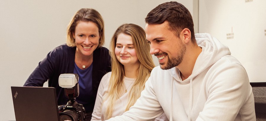 Eine Person schaut lächelnd auf einen Laptop. Zwei weitere Personen schauen ebenfalls auf den Laptop. Foto: Thomas Grimm