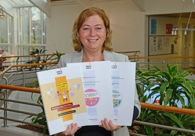 Die Heftreihe "Behinderungen im Fokus", präsentiert von Daniela Heimann. Foto: Judith Wedderwille/ Kreis Soest Daniela Heimann hält mehrere Hefte der Reihe "Behinderungen im Fokus" in der Hand und lächelt. Foto: Judith Wedderwille/ Kreis Soest