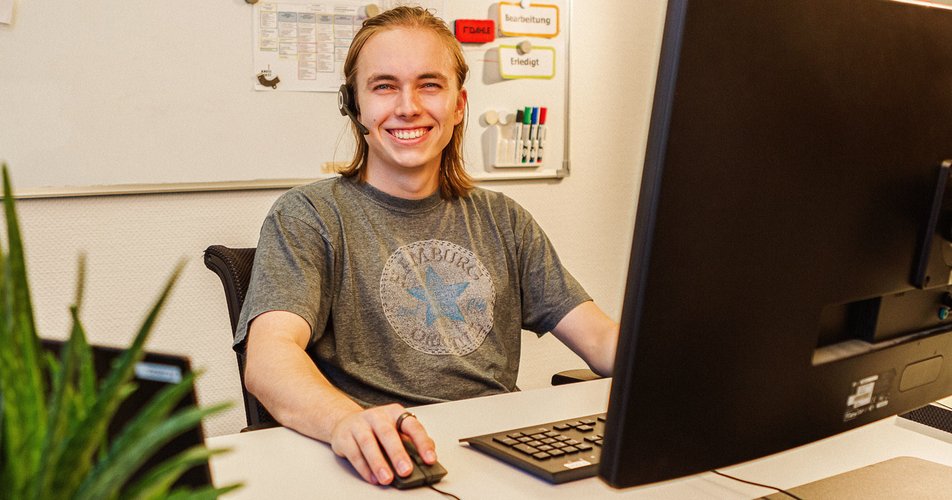 Fachinformatiker - Systemintegration. Foto: Thomas Grimm Ein junger Mann sitzt vor einem großen Bildschirm und lächelt in die Kamera. Foto: Thomas Grimm