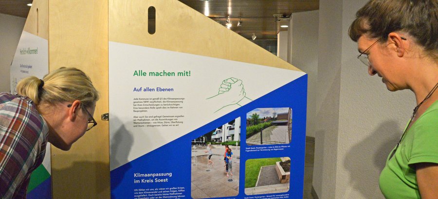 Aufsteller zur Ausstellung „Aufgepasst. Angepasst!“. Foto: Kira Hönicke/ Kreis Soest Bei Personen betrachten den Aufsteller zur Ausstellung „Aufgepasst. Angepasst!“. Foto: Kira Hönicke/ Kreis Soest