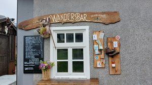 Ein Fenster, über dem "Wanderbar" steht, daneben eine Getränkekarte und Wander-Accessoires. 