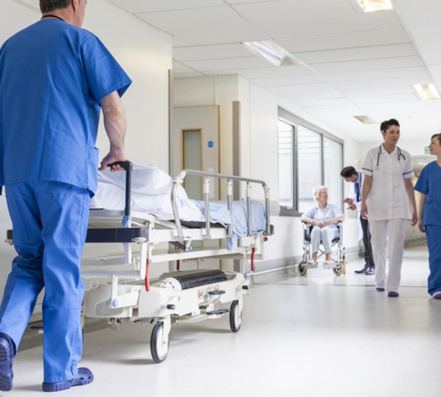 Krankenhausmitarbeiter schiebt Bett durch einen Krankenhausflur.  Foto: © spotmatikphoto - Fotolia