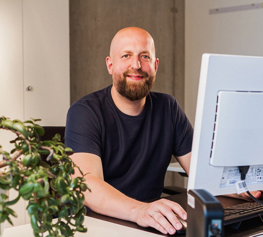 Ein Mann sitzt vor einem PC und lächelt in die Kamera. Foto: Thomas Grimm