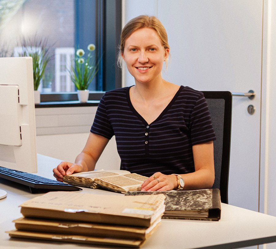 Eine junge Frau hat mehrere alte Akten vor sich liegen. Foto: Thomas Grimm