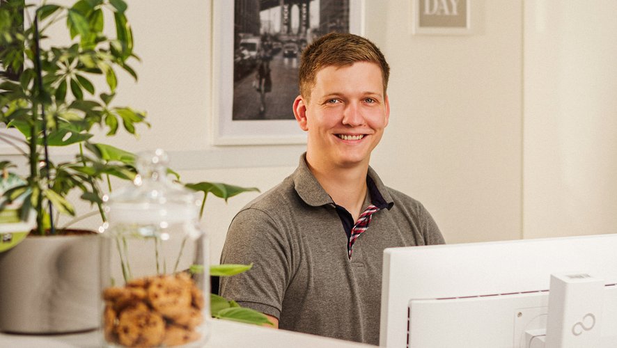 Ein Mann sitzt an seinem Arbeitsplatz und lächelt in die Kamera. Foto: Thomas Grimm